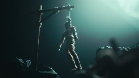 a miniature mummified doll hanging on the gallows at night