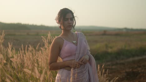 woman in traditional sari standing thoughtfully in a golden field at dusk, gentle breeze, serene expression