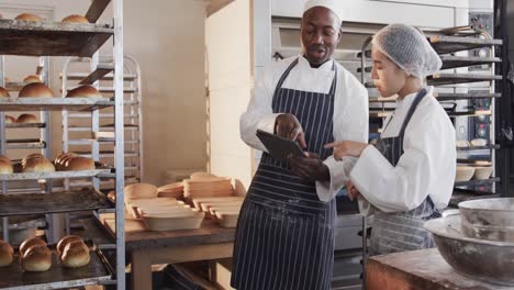 diverse female and male bakers working in bakery kitchen, using tablet, slow motion