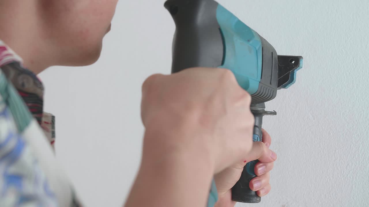 las manos del hombre usan un taladro eléctrico para perforar la pared