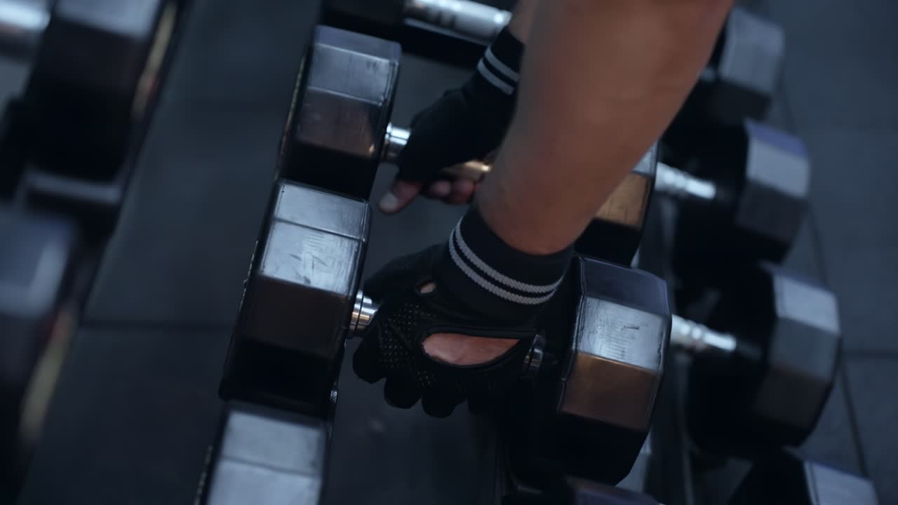 Man hands taking dumbbells from shelf at the gym - close up