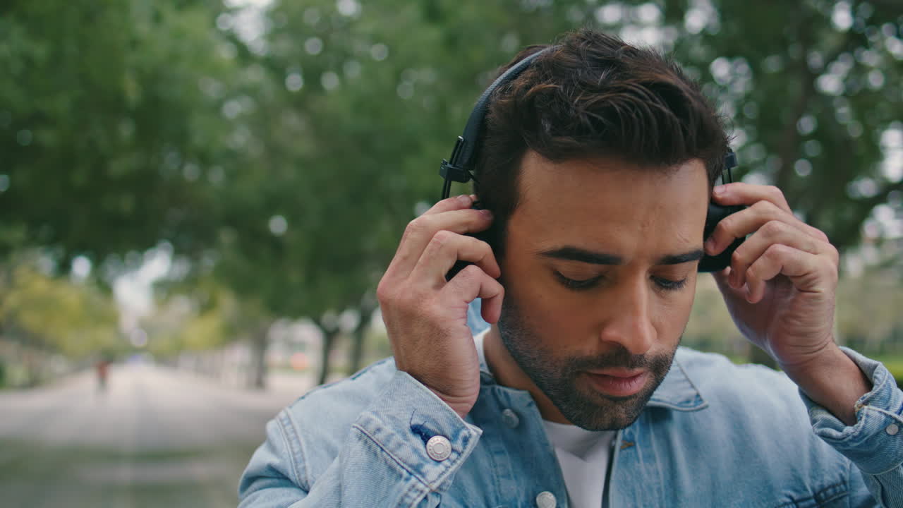 retrato de un tipo con auriculares en la calle verde. hombre italiano poniendo auriculares