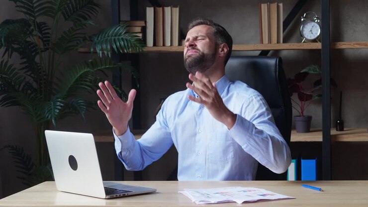 A businessman in a blue shirt looks at the laptop screen with concentration and expresses an emotion of annoyance. The company is defeated or the deal is not successful