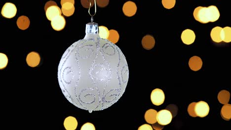 adorno de bola de navidad blanco único con rayas de brillo plateado y luces fuera de foco parpadeando en el fondo, cerrar