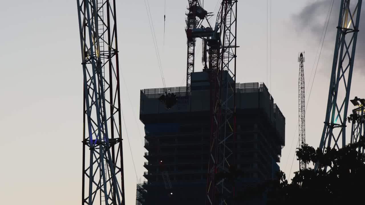 Silhouetted thrill ride swings between towers above cityscape, dusk lighting, static wide shot