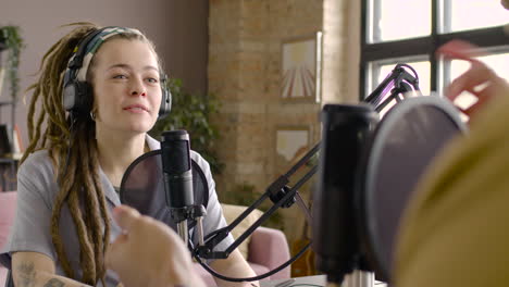 woman sitting at a table with microphones while recording a podcast with man