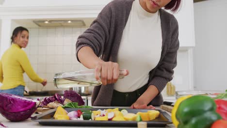 happy biracial sisters cooking dinner together in kitchen, in slow motion