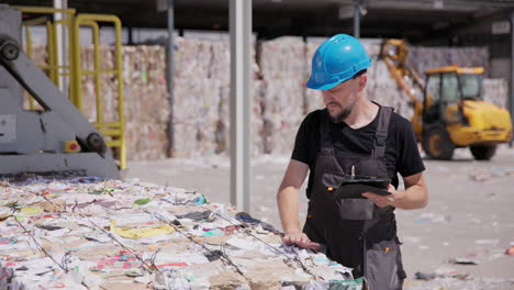 hombre con sombrero duro con tableta controla las balas de papel en la instalación de reciclaje