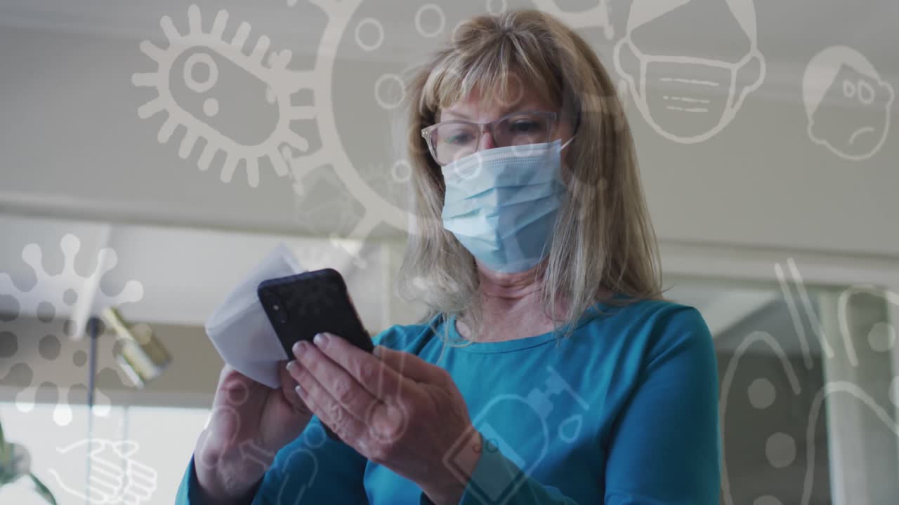 animación de iconos de covid 19 sobre una mujer caucásica mayor que usa una máscara facial desinfectando un teléfono inteligente