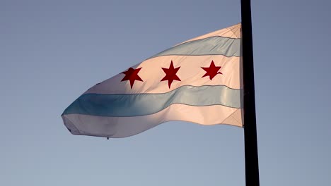 Die-Chicago-Flagge-Weht-An-Einem-Windigen-Tag-Mit-Morgendlichen-Sonnenstrahlen,-Die-Auf-Dem-Fahnenmast-Durchscheinen