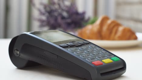 close up young woman at cafe buy breakfast food croissant hold wireless modern bank payment terminal to process acquire credit card payments at store checkout.