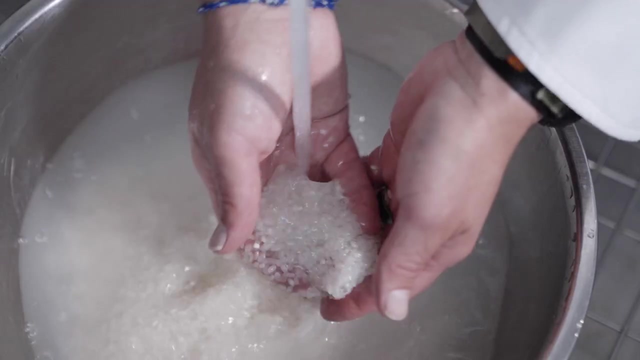Toma estática cenital de un chef enjuagando arroz con agua en un tazón. Perfecta para contenido culinario, destacando el proceso de lavado del arroz y la importancia de la preparación de ingredientes.
