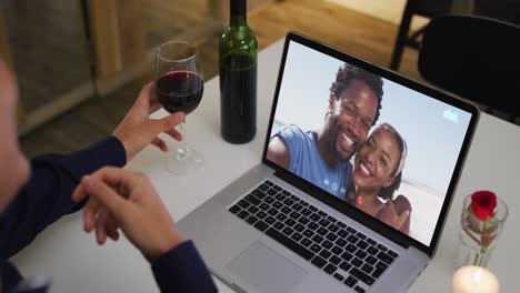 Mixed-race-man-sitting-at-table-using-laptop-making-video-call-with-friends