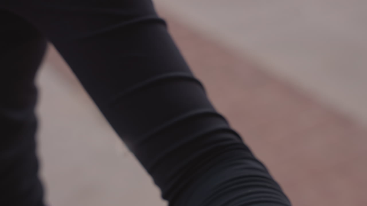 close up arm in black sleeve showing fabric texture and slight movement, athlete warming up outdoors on pavement, focused preparation with wrist and elbow details and fitted top creases