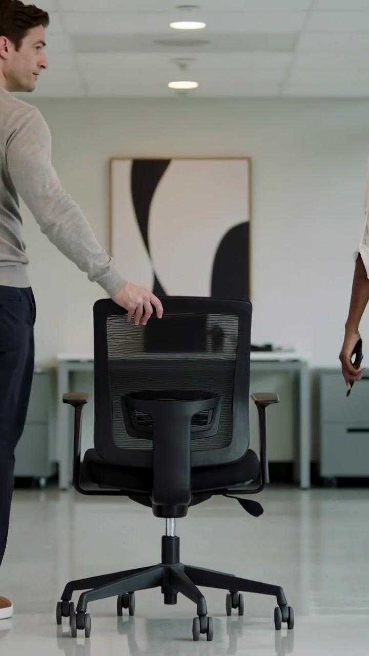 Video verticale: Uomo che si allunga e tiene lo schienale di una sedia da ufficio in rete in ufficio, donna che entra con il telefono