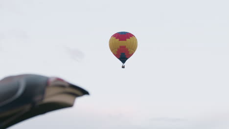open car trunk hatch framing distant colorful hot air balloon floating above grassy field under soft pastel evening sky, trunk storage area unpacked gear visible beside parked suv