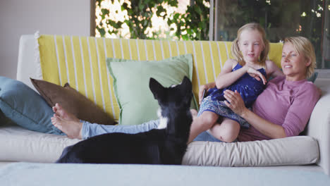 side view of caucasian woman and her daughter playing with the dog at home