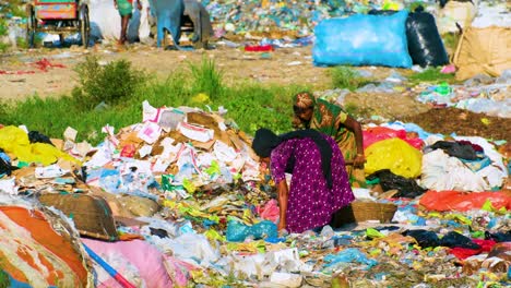 two woman dig through a garbage pile in a landfill with metal rakes in bangladesh