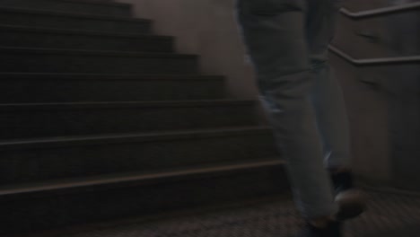 El-Joven-Está-Corriendo-Escaleras-Arriba-Con-Zapatillas-Y-Jeans-Geniales,-De-Mano