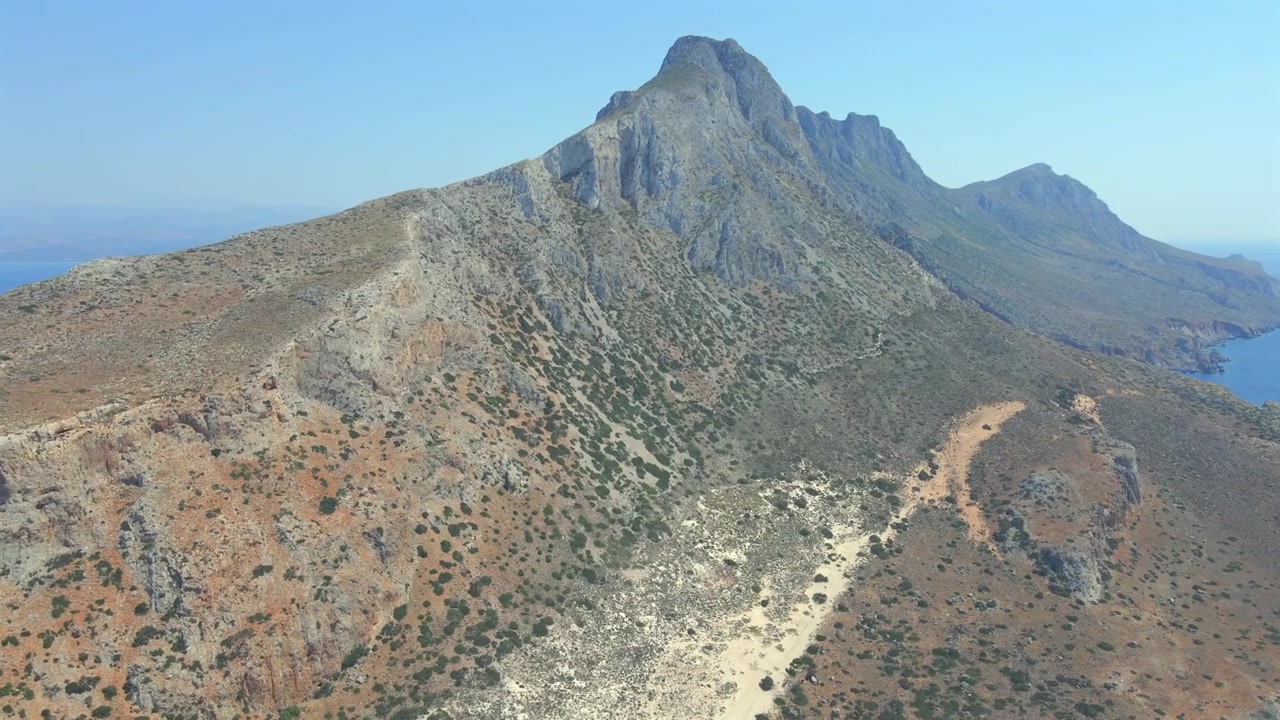 Splendida ripresa grandangolare con drone che mostra le aspre montagne rocciose e la cresta affilata della penisola di Gramvousa a Creta, Grecia. Caratterizzata da terreno selvaggio e arido e mare blu profondo a lato, giornata di sole.