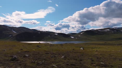 aerial low flying over tranquil lake surrounded by mountain terrain with scattered clouds in the blue sky, depicting nature's peace and beauty in perfect harmony