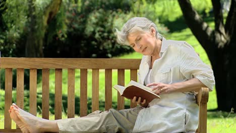 Elderly-female-reading-a-book-sitting-on-a-bench