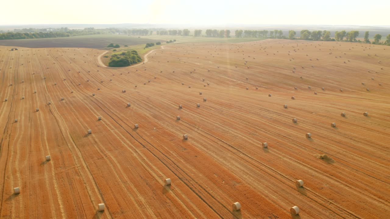 Drone flying above picturesque farmland with golden haystacks on a sunny day.