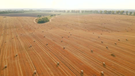 drone flying above picturesque farmland with golden haystacks on a sunny day.