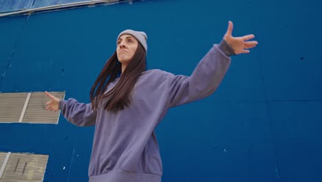 woman in urban fashion posing against a blue wall