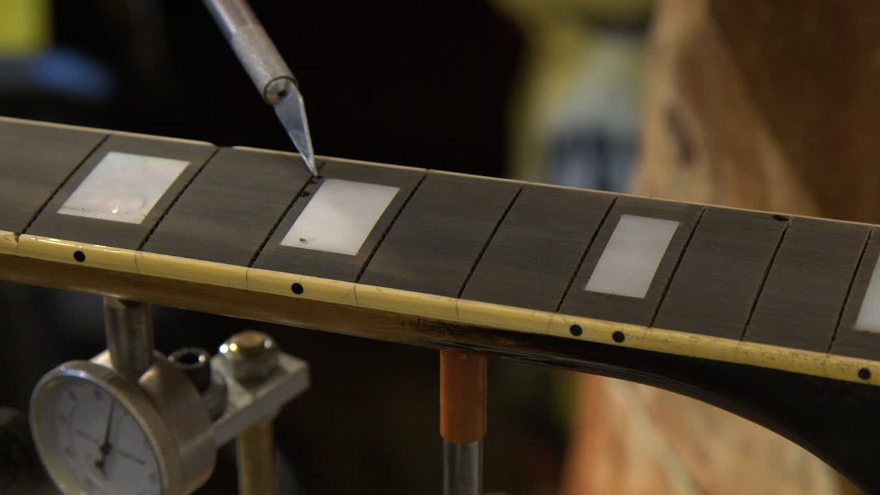 Primer plano de técnico de guitarra aplicando masilla en el diapasón de ébano de una guitarra.