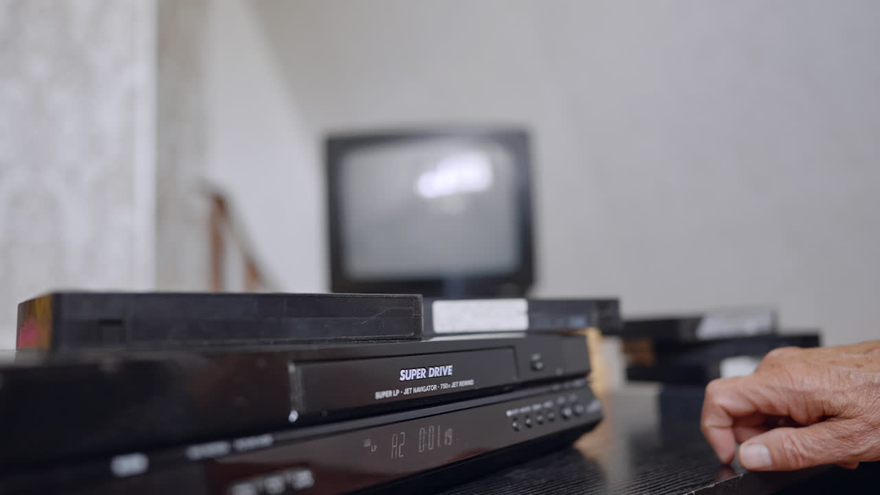 Hand operating VCR control panel. A person presses a control button on a vintage VCR placed beneath a blurred TV screen