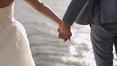 newlyweds are standing by the sea. they give each other hands. groom and bride