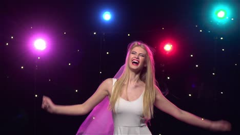 blonde woman dancing in a wedding dress with colorful lights