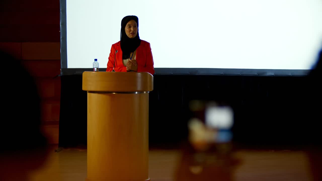 Mature Caucasian hijab businesswoman speaking at podium in auditorium 4k