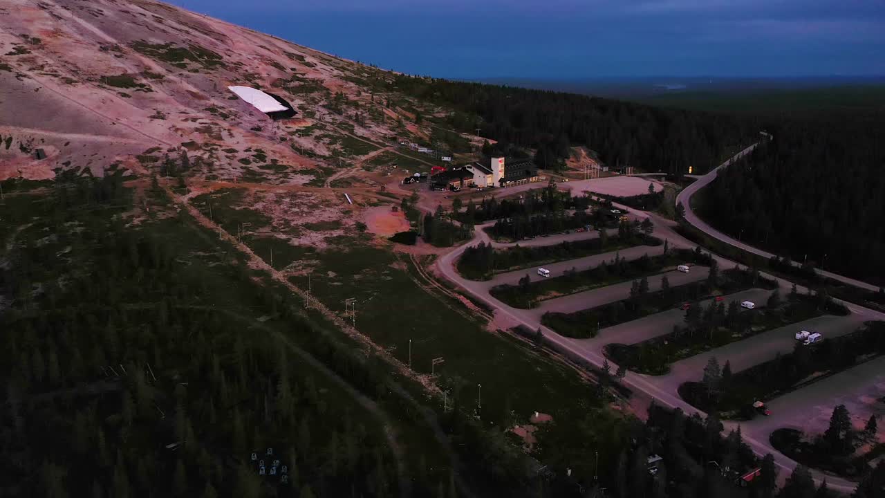 Aerial view of the Yllas fell and ski shop, on a colorful, summer dusk, during midnight sun, in Pallas-Yllastunturi national park, Kolari, Lapland, Finland - descending, dolly, drone shot