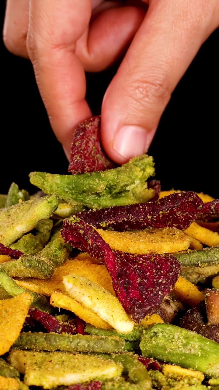 Una mano umana seleziona una chips di barbabietola essiccata da un assortimento di chips di verdure croccanti sotto una luminosa illuminazione da studio