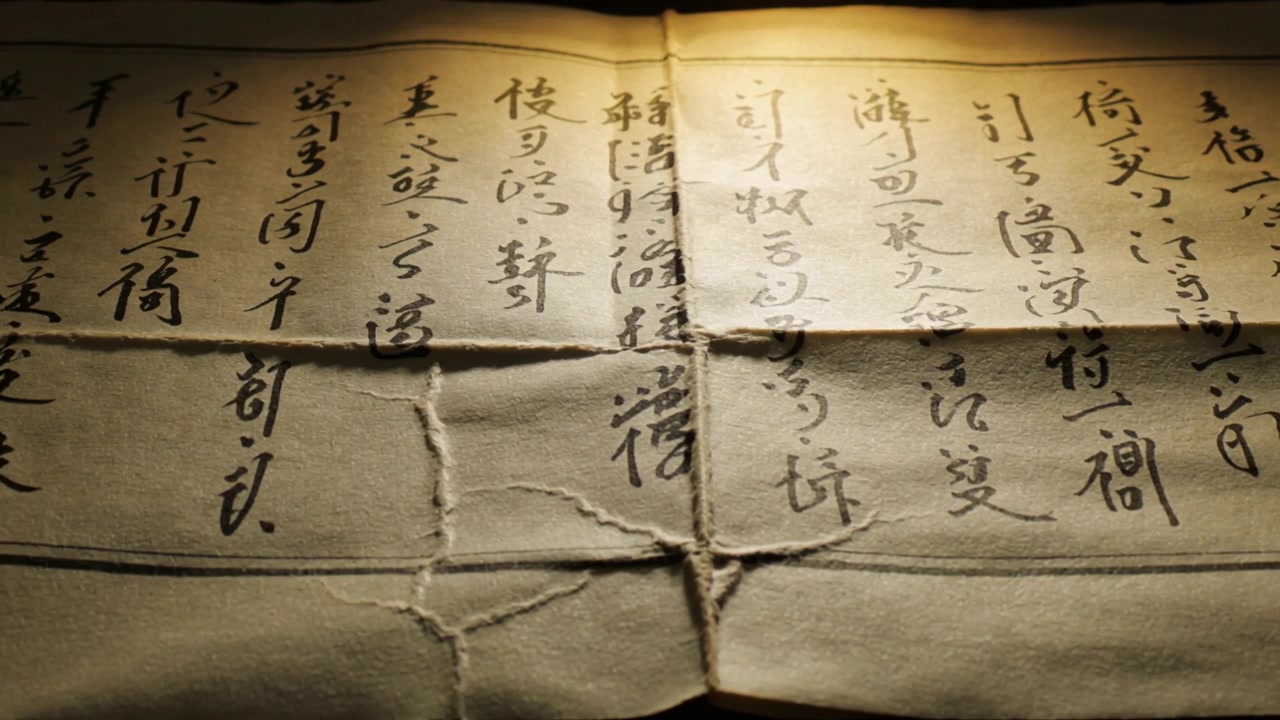 Panning camera revealing aged paper on dark table under warm lamp, showing ink columns, torn fold