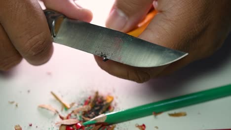 imágenes de manos afilando lentamente un lápiz y algunos lápices de colores con un cuchillo afilado