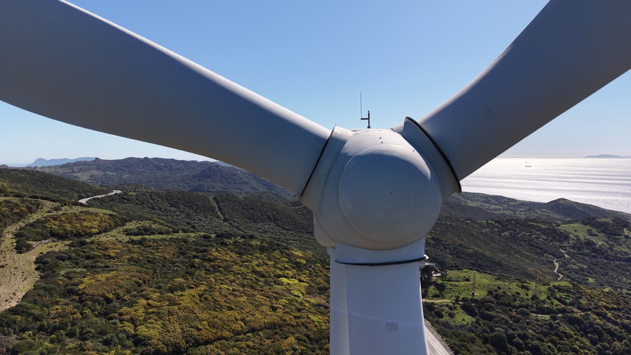 Close-up drone shot rotating around the hub of a wind turbine, with the straits of Gibraltar in the background