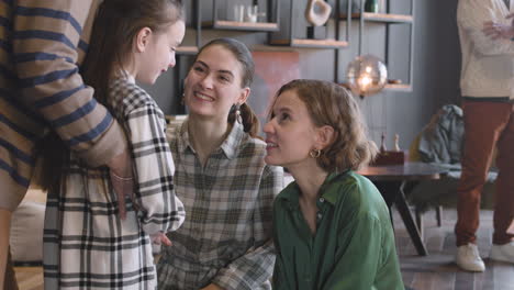 Little-Girl-Talking-With-Her-Happy-Mother-And-Aunt-While-Unrecognizable-Grandmother-Hugging-Her-From-Behind-During-A-Family-Reunion-At-Home