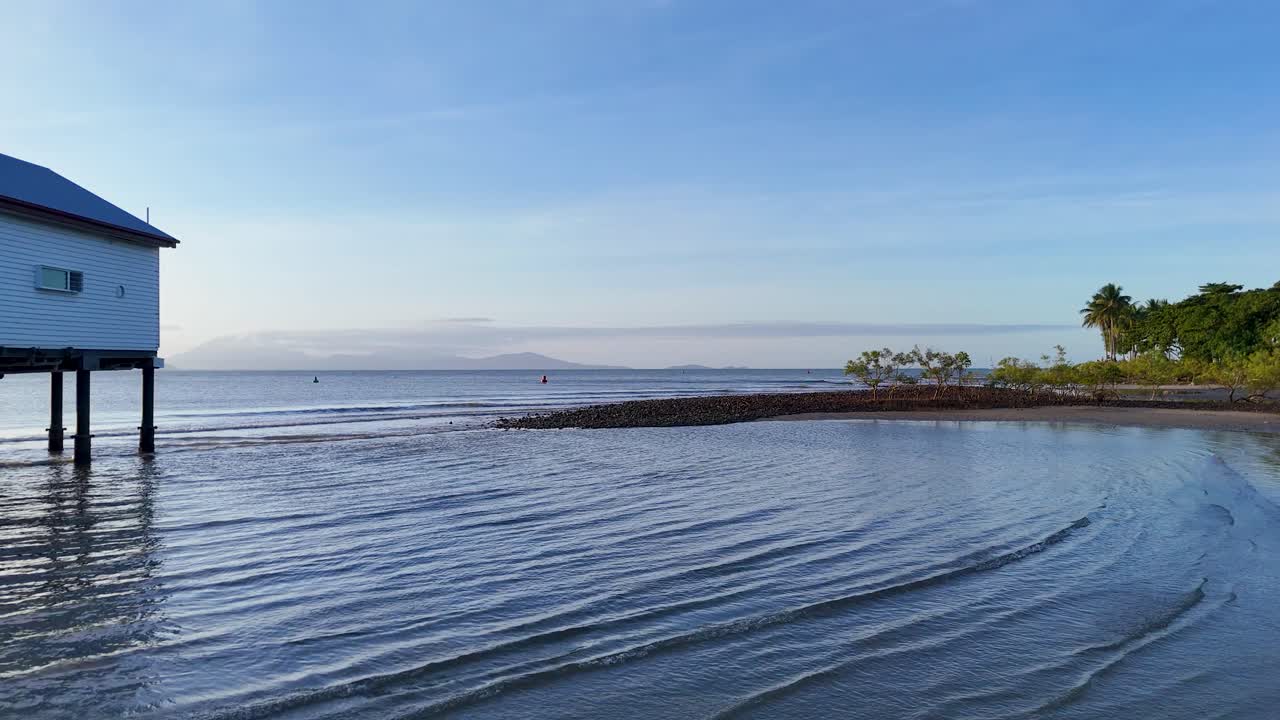 Drone captures serene coastal house, mangroves, and calm waters under clear skies with gentle camera movement