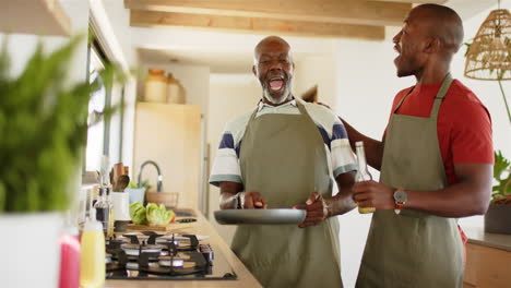 cooking together in kitchen, african american father and son wearing aprons and enjoying drinks