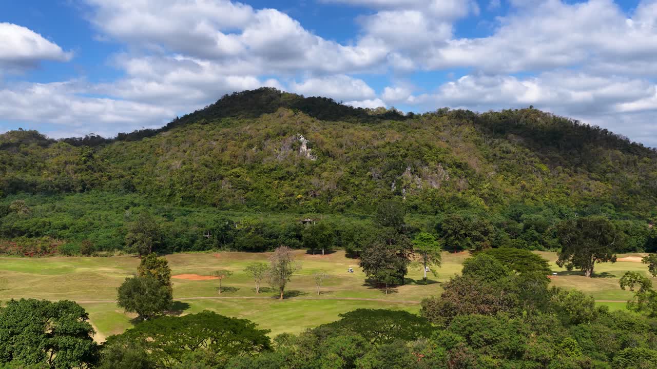 La videocamera di un drone si alza sopra alberi rigogliosi rivelando un pittoresco fairway di un campo da golf e montagne in lontananza