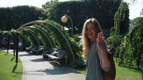 joyful caucasian women wants us to follow her through city park path on a beautiful sunny day