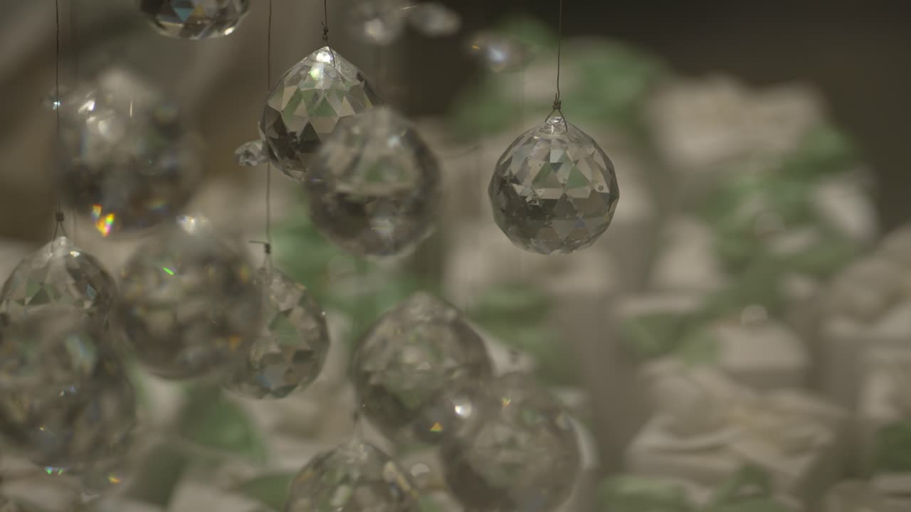 Faceted crystal ornaments hang above blurred white and green wedding favors in soft focus