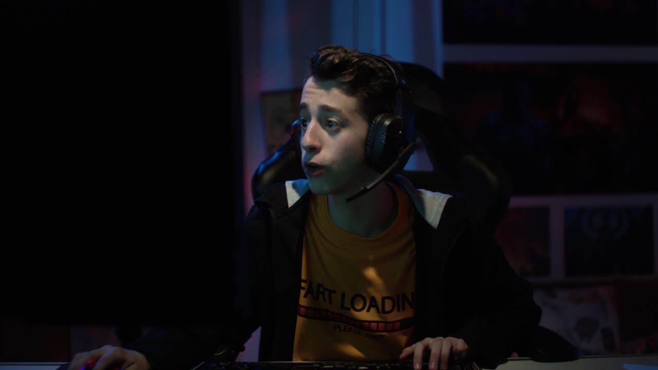 Teenage Gamer Speaking On The Headset While Playing On The PC In The House At Night - medium shot, slow motion