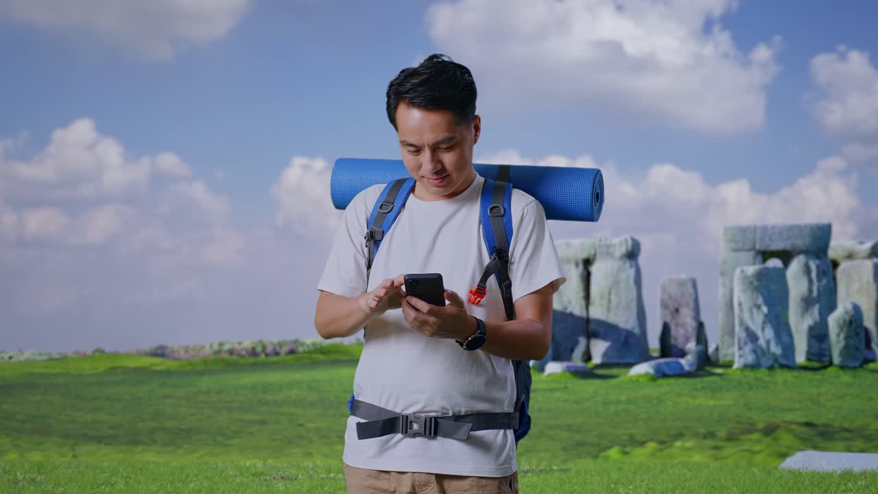Asian Male Hiker With Mountaineering Backpack Enjoy Using Smartphone While Traveling In Stonehenge