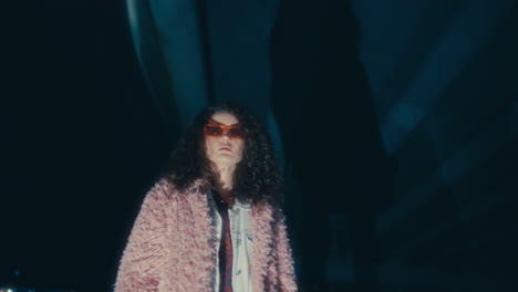 portrait of trendy woman in sunglasses under road bridge at night