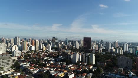 traveling-backwards-with-drone-filming-many-buildings-in-city-with-blue-sky-in-4K-resolution