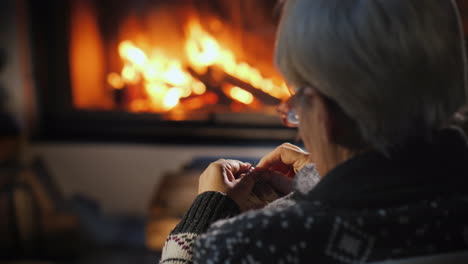 ältere dame strickt einen warmen schal am kamin